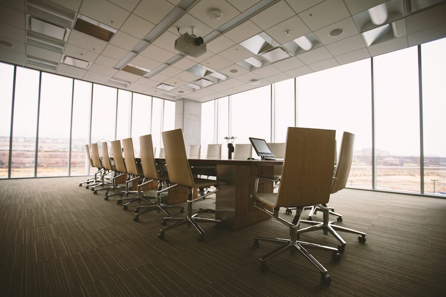 An empty boardroom with a long table and city light through the windows